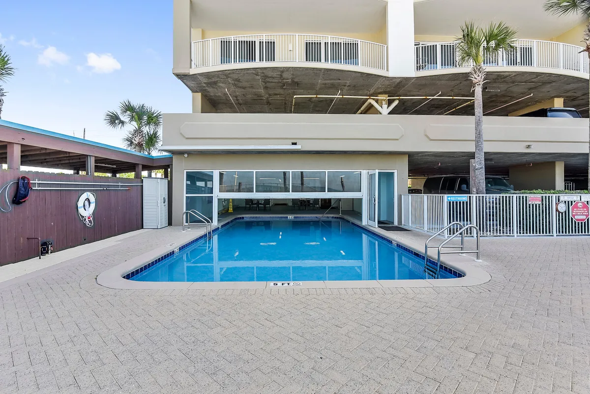 The resort’s inviting swimming pool area is the focal point, framed by palm trees and surrounding resort architecture. Guests are seen enjoying the water and lounging, with the sun casting a warm, energetic glow on the deck area.