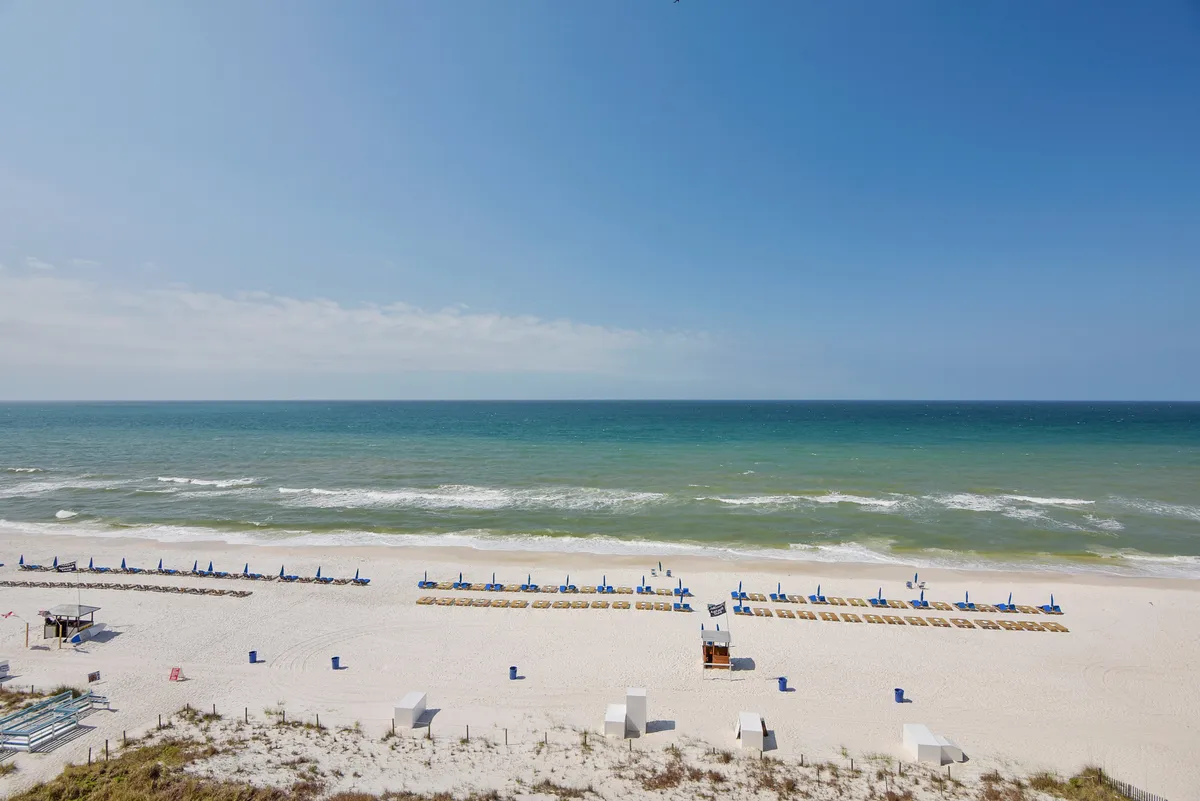 This image depicts a stretch of sandy beach with blue ocean waves in the background and several beach chairs and umbrellas set up along the shore. The sky is clear, and the atmosphere is tranquil and inviting, suggesting an ideal place for families to enjoy endless beach days.