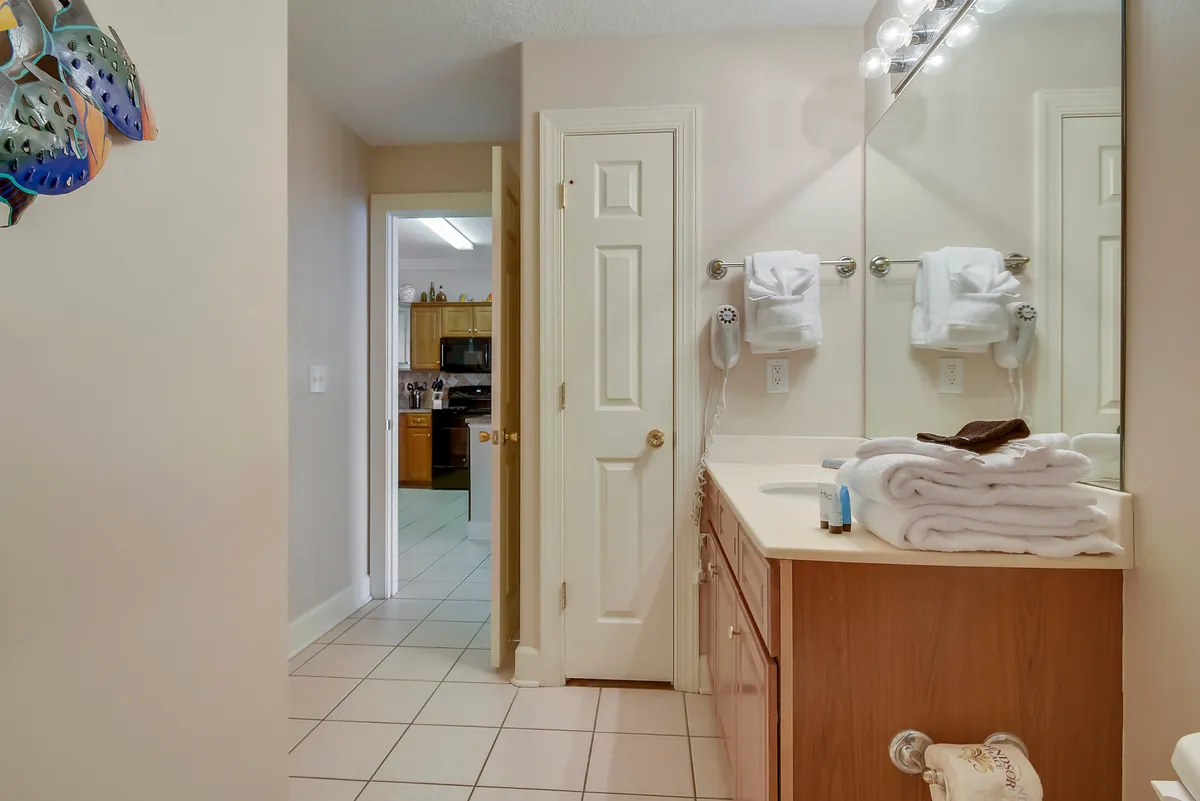 A bathroom featuring a mirror, vanity, towels, and shelves with decorative items. The space is calm and organized, perfect for personal grooming and relaxation after a day in the sun.