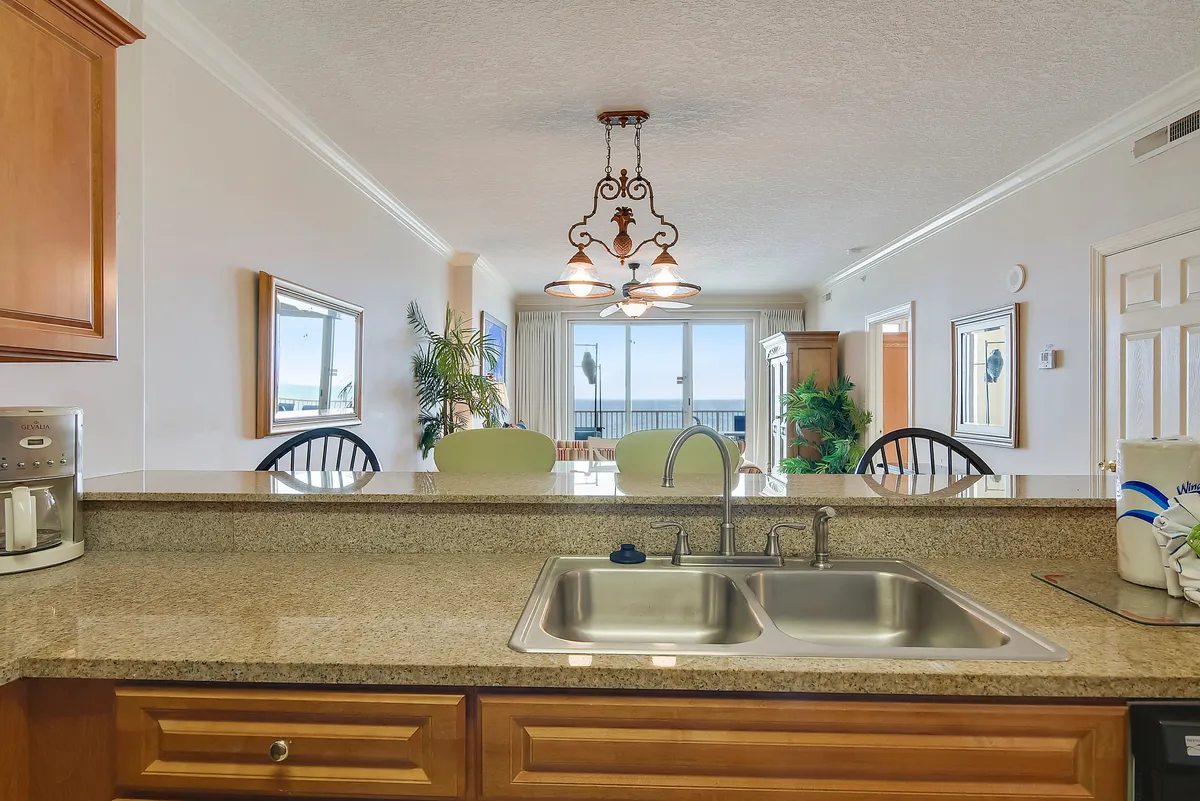 A dining area seamlessly connected to the kitchen, featuring a granite countertop, elegant chandelier, and large windows with stunning ocean views. The setup is ideal for enjoying meals with family or hosting friends, combining luxury with comfort.