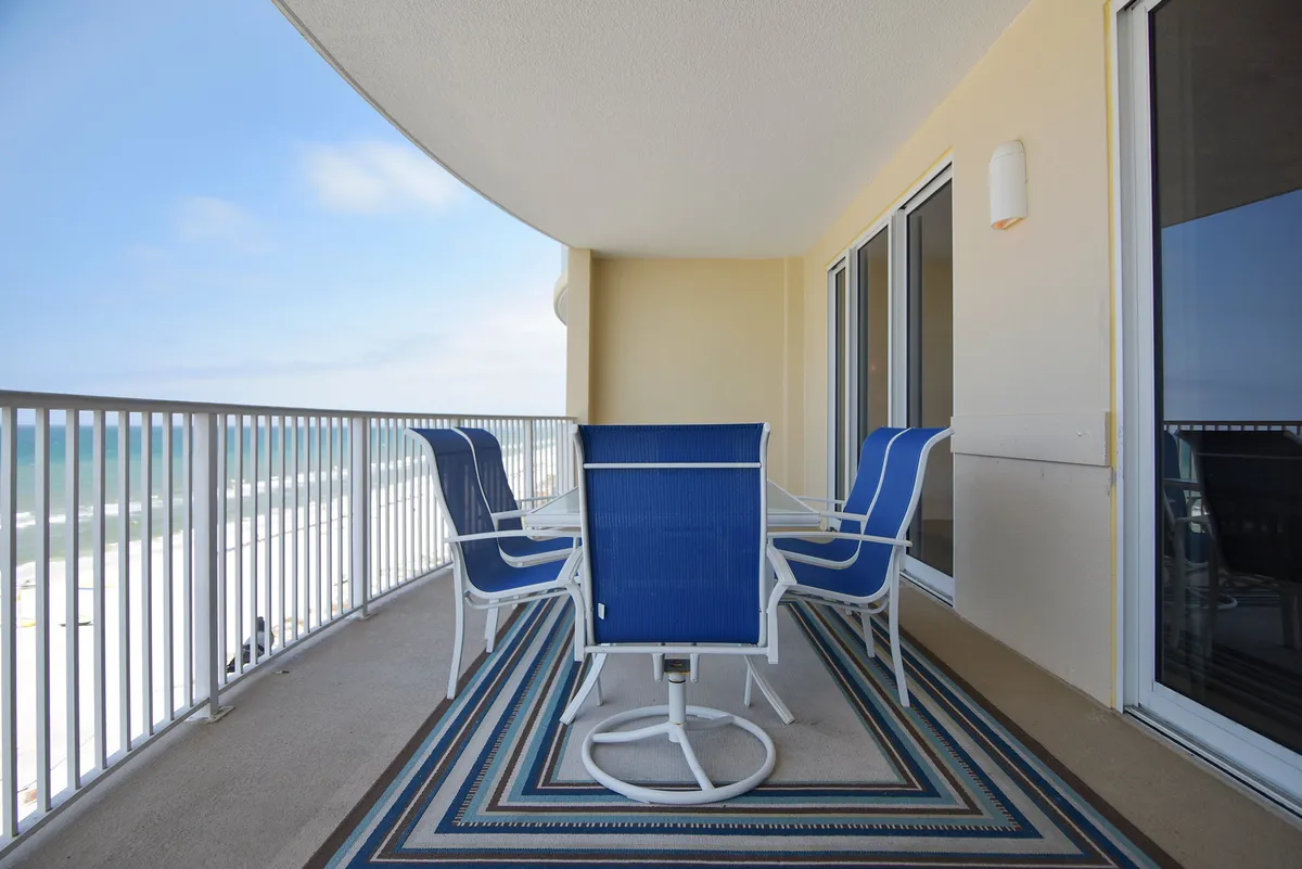A tranquil balcony setup with comfortable seating and a decorative rug overlooks the ocean. The scene suggests a private, serene spot for enjoying morning coffee or evening cocktails while taking in sweeping seaside views.