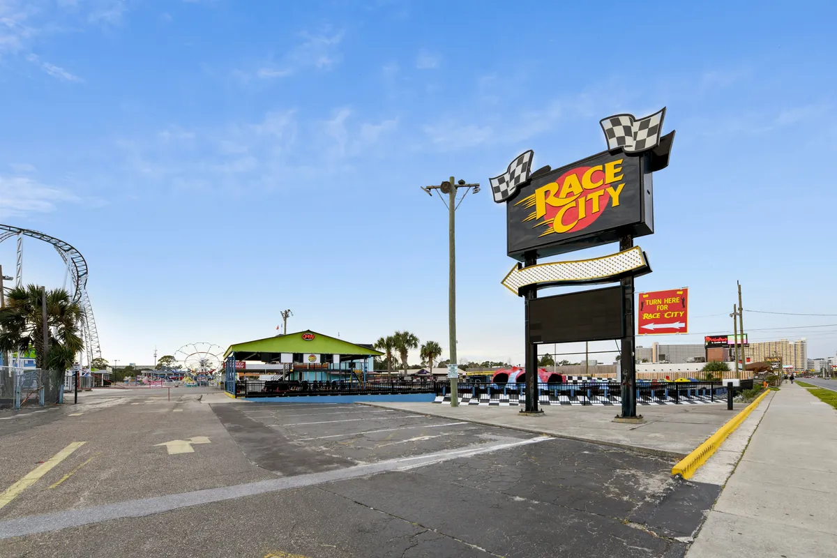 This image captures the energetic atmosphere of Race City, with a prominent sign marking the entrance, a visible go-kart track, and vibrant amusement rides in the background. Outdoor seating and social spaces add to the lively scene, inviting guests to participate in adventure and recreation.