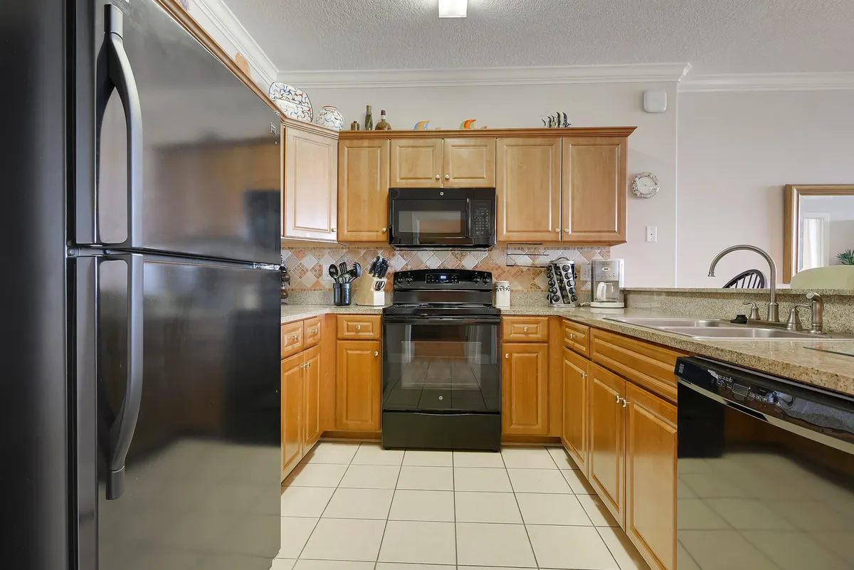 A cozy, well-equipped kitchen with a black refrigerator, stove, microwave, wooden cabinets, and a spacious sink area. The layout allows for easy meal preparation and group cooking.