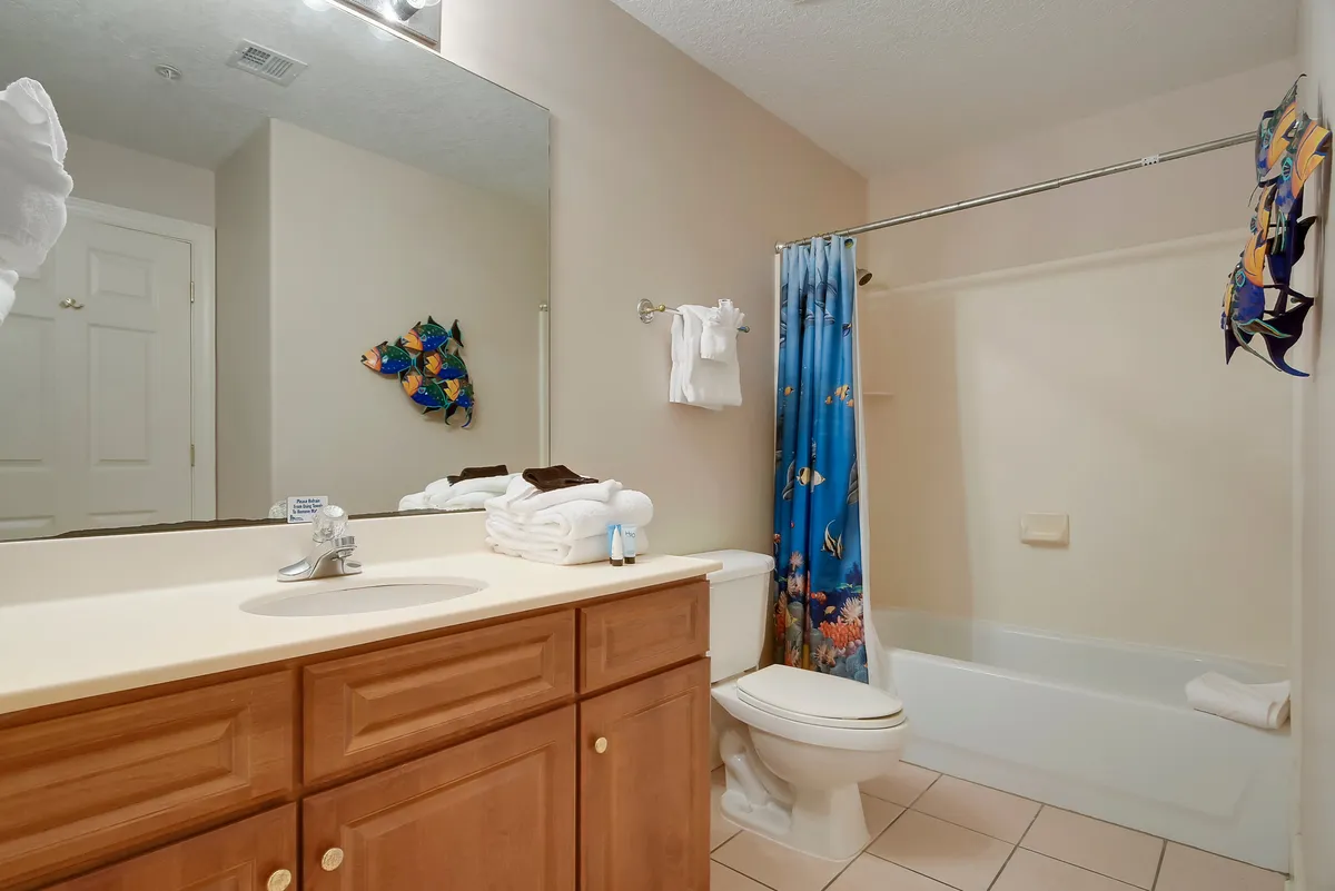 A bright, functional bathroom with a large mirror above the sink, a bathtub with ocean-themed shower curtain, and a wooden vanity with countertop. The overall look is clean, inviting, and practical for family use.
