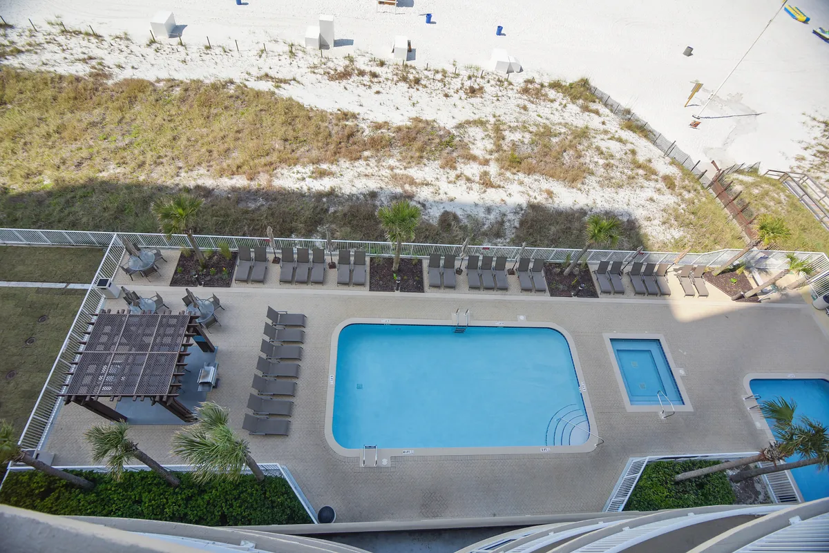 A sparkling rectangular swimming pool and adjacent hot tub are set against a sandy beachfront with sparse vegetation. Lounge chairs line the poolside, offering spaces for sunbathing, socializing, or simply soaking in the tranquil ocean view. The scene exudes relaxation and resort luxury.