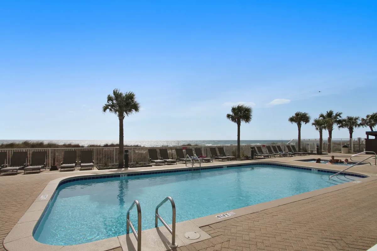 An outdoor swimming pool with sparkling blue water sits alongside a row of palm trees and beach chairs, all facing the ocean horizon. The scene suggests a relaxing, leisure-filled resort environment with easy transitions between swimming, sunbathing, and enjoying the sea view.